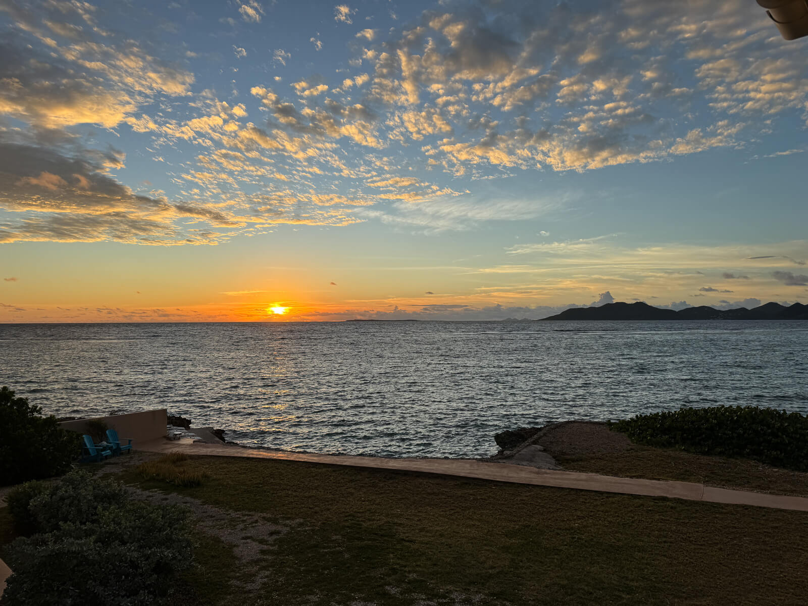 Sunset view from Villa Bénie — distant silhouette of St. Martin on the horizon, warm golden light over calm water